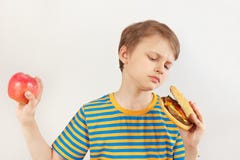 Young boy chooses between hamburger and apple on white background stock photography Young boy chooses between hamburger and apple on white background stock photography