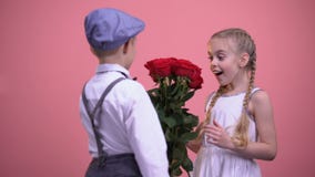 Young boy in formal clothes hiding roses behind back and presenting to girl stock video footage Young boy in formal clothes hiding roses behind back and presenting to girl stock video footage