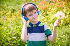 Young boy in headphones listening to modern music in nature. Child likes the song and look to giant dandelion. Kid music relax
