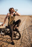 Young brutal man sitting on his motorcycle and drinking water stock image Young brutal man sitting on his motorcycle and drinking water stock image