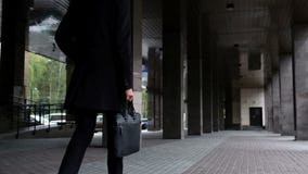 Young businessman lawyer in classic costume and a coat hold case with documents and walk slow motion. He walks down the