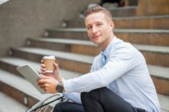 Young businessman sitting on the stairs with bicycle holding paper coffee cup and tablet taking a rest and relaxing on street in royalty free stock photography Young businessman sitting on the stairs with bicycle holding paper coffee cup and tablet taking a rest and relaxing on street in royalty free stock photography