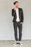 A young businessman with a smile is standing by the wall and talking on the phone stock photography A young businessman with a smile is standing by the wall and talking on the phone stock photography