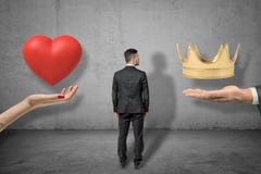 Young businessman standing between two big hands holding red heart and golden crown on grey wall background. background royalty free stock images Young businessman standing between two big hands holding red heart and golden crown on grey wall background. background royalty free stock images