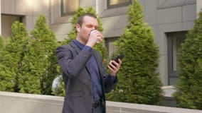 Young businessman walking down the street with wireless earphones in the ears and writes a message on the phone stock video footage Young businessman walking down the street with wireless earphones in the ears and writes a message on the phone stock video footage