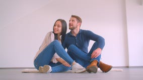 Young caucasian couple sitting on floor of new apartment hugging and kissing being happy. stock footage Young caucasian couple sitting on floor of new apartment hugging and kissing being happy. stock footage