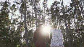Young couple hold the hands and walking in a pine forest in the background of sunshine. Couple spends leisure time stock video Young couple hold the hands and walking in a pine forest in the background of sunshine. Couple spends leisure time stock video