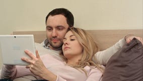 Young couple lying on the bed make shopping over the Internet using tablet using tablet computer stock photos Young couple lying on the bed make shopping over the Internet using tablet using tablet computer stock photos