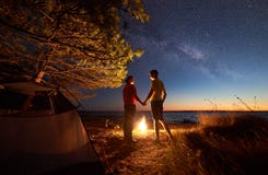Young couple man and woman having rest at tourist tent and burning campfire on sea shore near forest royalty free stock image Young couple man and woman having rest at tourist tent and burning campfire on sea shore near forest royalty free stock image