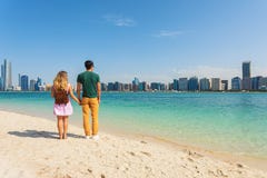 Young couple of tourists holding hands on beach looking at the modern buildings from Abu Dhabi. Honeymoon excursion and summer tra stock images Young couple of tourists holding hands on beach looking at the modern buildings from Abu Dhabi. Honeymoon excursion and summer tra stock images