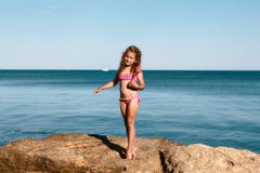 Young curly girl in a pink swimsuit relaxing on the rocks on the beach, standing on her fingers Black Sea, Odessa, Ukraine, place royalty free stock image Young curly girl in a pink swimsuit relaxing on the rocks on the beach, standing on her fingers Black Sea, Odessa, Ukraine, place royalty free stock image
