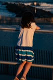 Young cute little girl on the boardwalk with back to camera looking towards the ocean surf royalty free stock photos Young cute little girl on the boardwalk with back to camera looking towards the ocean surf royalty free stock photos