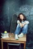 Young Cute Teenage Girl In Classroom At Blackboard Seating On Table Smiling, Modern Hipster Concept Royalty Free Stock Image