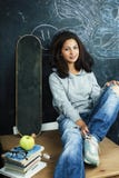 Young Cute Teenage Girl In Classroom At Blackboard Seating On Table Smiling, Modern Hipster Concept Stock Photo
