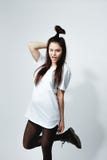 Young dark-haired girl with a funny hairstyle dressed in white t-shirt, black tights and shoes winks posing on the white royalty free stock photography Young dark-haired girl with a funny hairstyle dressed in white t-shirt, black tights and shoes winks posing on the white royalty free stock photography