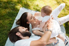 Young dark-haired mother and father dressed in white clothes are lying on a striped plaid on a law holding in the arms royalty free stock photos Young dark-haired mother and father dressed in white clothes are lying on a striped plaid on a law holding in the arms royalty free stock photos