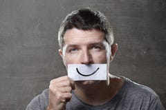 Young depressed man lost in sadness and sorrow holding paper with smiley on his mouth in depression concept Royalty Free Stock Images Young depressed man lost in sadness and sorrow holding paper with smiley on his mouth in depression concept Royalty Free Stock Images