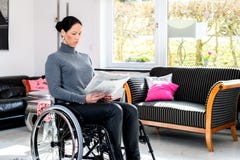 Disabled woman in wheelchair at home reading newspaper and drink stock image Disabled woman in wheelchair at home reading newspaper and drink stock image
