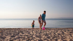 Young family playing football on the beach. Young family frolicking together playing football soccer on the beach at sunset with the little boy running with his Young family playing football on the beach. Young family frolicking together playing football soccer on the beach at sunset with the little boy running with his