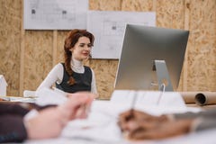 young female architect working with computer at office while colleagues drawong plans Royalty Free Stock Image young female architect working with computer at office while colleagues drawong plans Royalty Free Stock Image