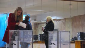 Young female blond voter puts the ballot in ballot box.