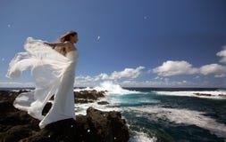 Young fiancee with white wings of wedding dress on rock sea shore on Sao Miguel island, Azores