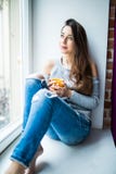A well-pleased young girl enjoying an ideal day sitting in the window-sill. Wearing casual denim jeans and blouse, crossing legs a. Young girl enjoying an ideal Royalty Free Stock Image A well-pleased young girl enjoying an ideal day sitting in the window-sill. Wearing casual denim jeans and blouse, crossing legs a. Young girl enjoying an ideal Royalty Free Stock Image