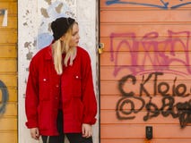 A young girl in a knitted hat and a red jacket stands against the painted wall of a garage stock photography A young girl in a knitted hat and a red jacket stands against the painted wall of a garage stock photography