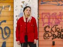A young girl in a knitted hat and a red jacket stands against the painted wall of a garage royalty free stock photo A young girl in a knitted hat and a red jacket stands against the painted wall of a garage royalty free stock photo