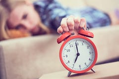 Young girl lies on the couch and stretches her hand to the red alarm clock to turn it off. Late wake up. stock photos Young girl lies on the couch and stretches her hand to the red alarm clock to turn it off. Late wake up. stock photos