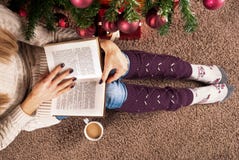 Young Girl Sitting On Floor And Reading Book Next To Christmas Tree And Coffee Cup Royalty Free Stock Photos