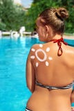 Young girl with sun shape from sunscreen lotion on her shoulder is resting near swimming pool with blue water. Summer time stock photography Young girl with sun shape from sunscreen lotion on her shoulder is resting near swimming pool with blue water. Summer time stock photography