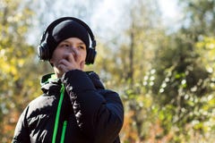 A young guy in a black hat and jacket covered his face with his hand and listened to music in headphones against the background of stock images A young guy in a black hat and jacket covered his face with his hand and listened to music in headphones against the background of stock images
