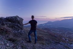 A young guy in a black T-shirt stands on top of a mountain, with his back to the camera and gazes sunse royalty free stock image A young guy in a black T-shirt stands on top of a mountain, with his back to the camera and gazes sunse royalty free stock image