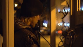 Young guy is calling and speaking in telephone booth at night city, cold weather.