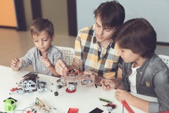 A young guy and two little boys are collecting robots. Around them are parts of different robots and mechanisms stock photo A young guy and two little boys are collecting robots. Around them are parts of different robots and mechanisms stock photo