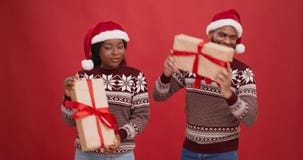 Young happy african american couple in Santa hats holding Xmas gifts and dancing over red studio background