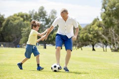 Young happy father and excited little 7 or 8 years old son playing together soccer football on city park garden running on grass k stock photos Young happy father and excited little 7 or 8 years old son playing together soccer football on city park garden running on grass k stock photos