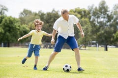 Young happy father and excited little 7 or 8 years old son playing together soccer football on city park garden running on grass k royalty free stock images Young happy father and excited little 7 or 8 years old son playing together soccer football on city park garden running on grass k royalty free stock images
