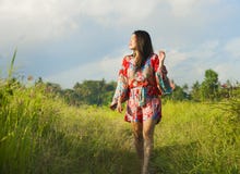 Young happy and playful Asian Chinese woman in beautiful dress having fun enjoying holidays excursion on grass tropical field smil Royalty Free Stock Images Young happy and playful Asian Chinese woman in beautiful dress having fun enjoying holidays excursion on grass tropical field smil Royalty Free Stock Images
