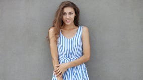 Young happy smiling beautiful woman in light dress with long brunette curly hair posing against wall on a warm Stock Photography Young happy smiling beautiful woman in light dress with long brunette curly hair posing against wall on a warm Stock Photography