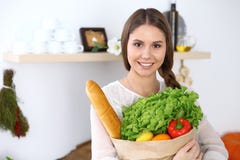 Young happy woman is holding paper bag full of vegetables and fruits while smiling in kitchen. Housewife have made Stock Photos Young happy woman is holding paper bag full of vegetables and fruits while smiling in kitchen. Housewife have made Stock Photos