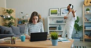 Young lady working with laptop at home while Arabian man dancing in background stock video Young lady working with laptop at home while Arabian man dancing in background stock video