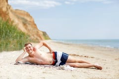 A young man at the beach background. A smiling guy lying on the sand near the blue ocean. Summer concept. Copy space. royalty free stock images A young man at the beach background. A smiling guy lying on the sand near the blue ocean. Summer concept. Copy space. royalty free stock images
