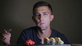 Young man eating sushi with chopsticks stock footage Young man eating sushi with chopsticks stock footage
