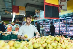 A young man gathers apples from the store shelves. A man buys fruit in the vegetable department of the supermarket. royalty free stock photos A young man gathers apples from the store shelves. A man buys fruit in the vegetable department of the supermarket. royalty free stock photos
