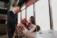 A young man gives a bouquet of red flowers to his girlfriend, wife, in a cafe by the window. stock photography A young man gives a bouquet of red flowers to his girlfriend, wife, in a cafe by the window. stock photography