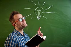 A young man with glasses is reading a book, an idea comes to mind on the background of a blackboard with a chalked light bulb stock photography A young man with glasses is reading a book, an idea comes to mind on the background of a blackboard with a chalked light bulb stock photography