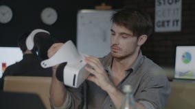 Young man holding virtual reality goggles in creative dark office stock footage Young man holding virtual reality goggles in creative dark office stock footage
