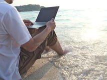 Young man with laptop sitting on sand of tropical beach during sunset time. Relax and travel concept. royalty free stock photos Young man with laptop sitting on sand of tropical beach during sunset time. Relax and travel concept. royalty free stock photos